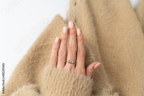 Graceful thin fingers of a girl with a trendy pastel nude manicure and a fluffy soft sweater and a cute silver ring bow