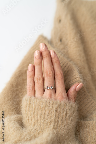 Graceful thin fingers of a girl with a trendy pastel nude manicure and a fluffy soft sweater and a cute silver ring bow