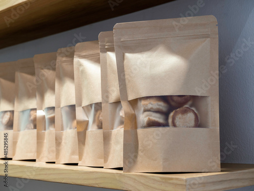 A row of blank craft paper bag packaging with soft cookies inside. Mockup template. Kraft paper zipper Pouch packaging for bakery snacks on wooden shelf. photo