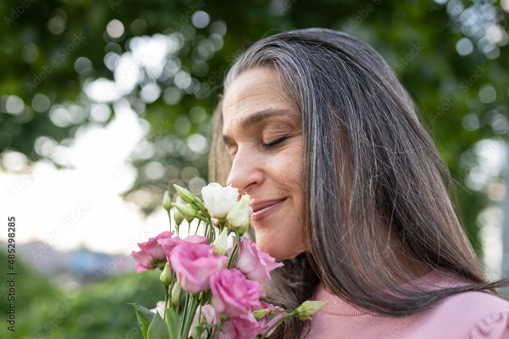 beautiful mature woman, with gray hair, smelling a bouquet of flowers on valentine's day beautiful mature woman, with gray hair, smelling a bouquet of flowers on valentine's day