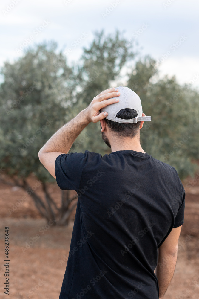 Rear view of a young man wearing black unbranded t-shirt and touching his grey hat