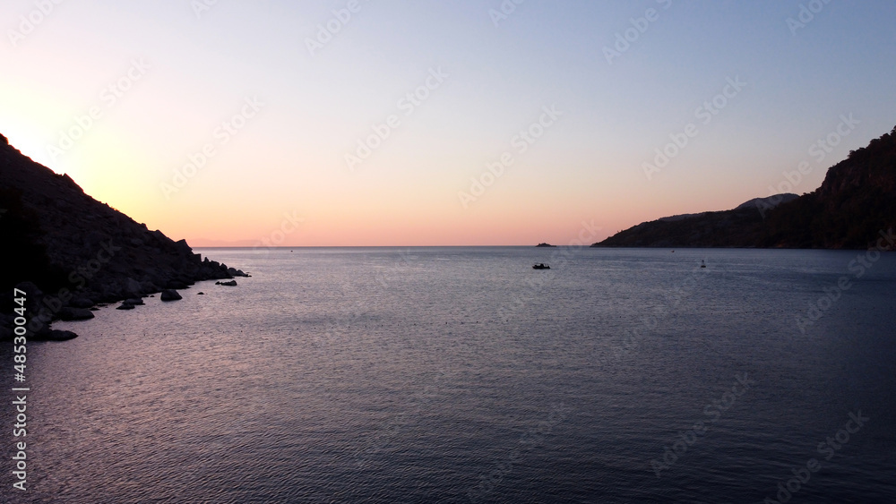 Sunrise over mountain rock in sea water. Sunrise seascape in calm sea. Rocks silhouette and golden reflections on the rippled water. Aerial drone view. Sunrise over mountain rock in sea water. Sunrise seascape in calm sea. Rocks silhouette and golden reflections on the rippled water. Aerial drone view.