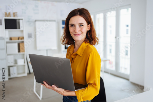 Smiling friendly young business manageress holding a laptop photo