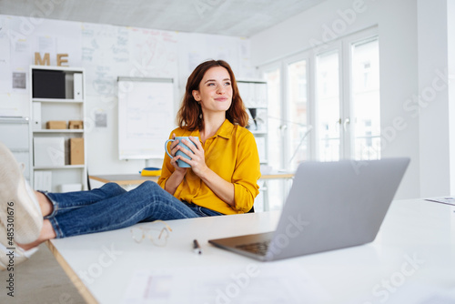 Happy young businesswoman sitting daydreaming in the office