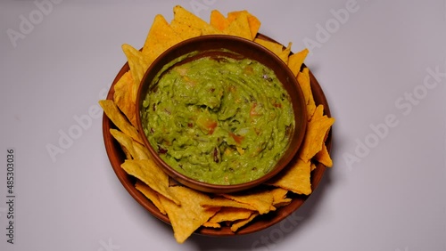 Man Hand taking some fried nachos in a pot with some fresh guacamole from clay dishes on white background. photo