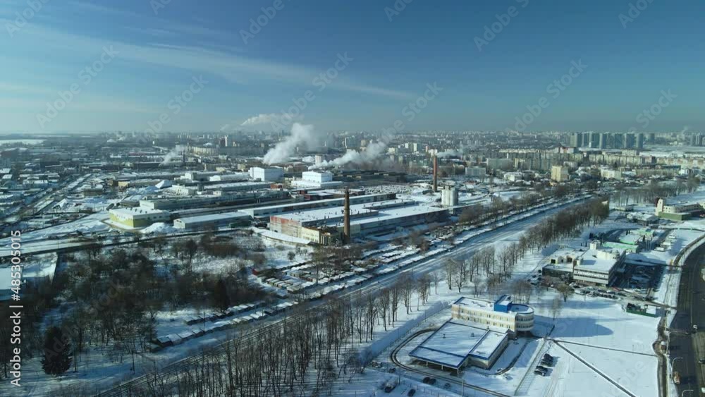 Factory buildings covered with snow. Factory smoke chimneys. There is a railway nearby. You can see the city blocks. Winter industrial landscape. Aerial photography.