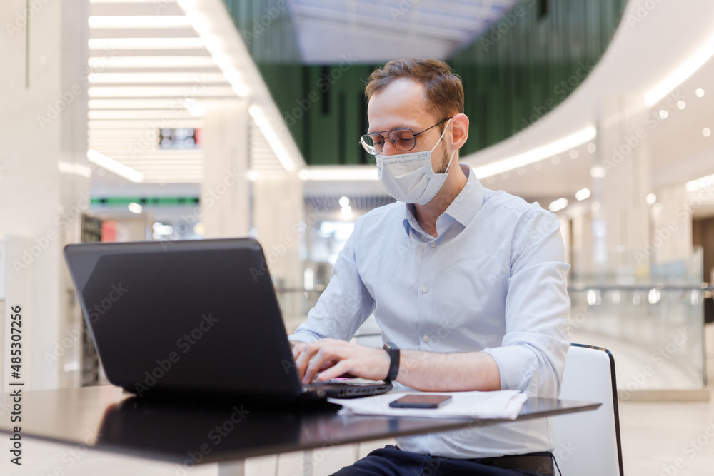 Clerk in face mask man working remotely on laptop in a public place Clerk in face mask man working remotely on laptop in a public place