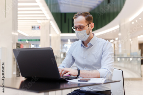 Clerk in face mask man working remotely on laptop in a public place
