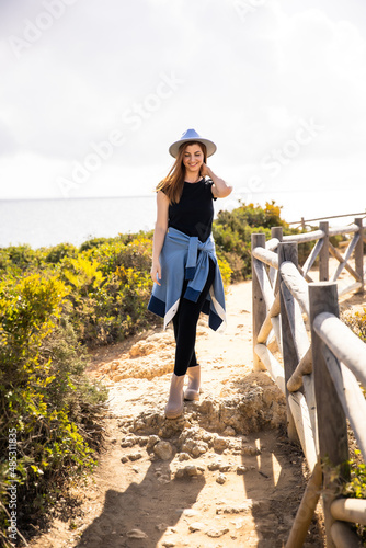 a young beautiful girl in a blue hat stands on a rock against the background of the beach and the ocean in Portugal © Alexander