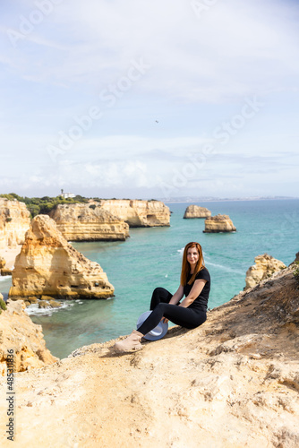 young beautiful girl in sits on a rock against the backdrop of the beach and the ocean in Portugal