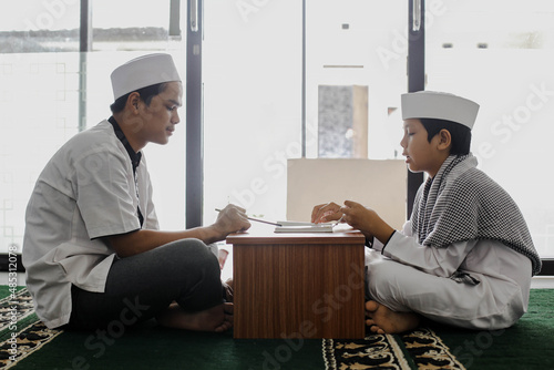 Side view of muslim teacher and student teaching how to read the Koran in the mosque photo