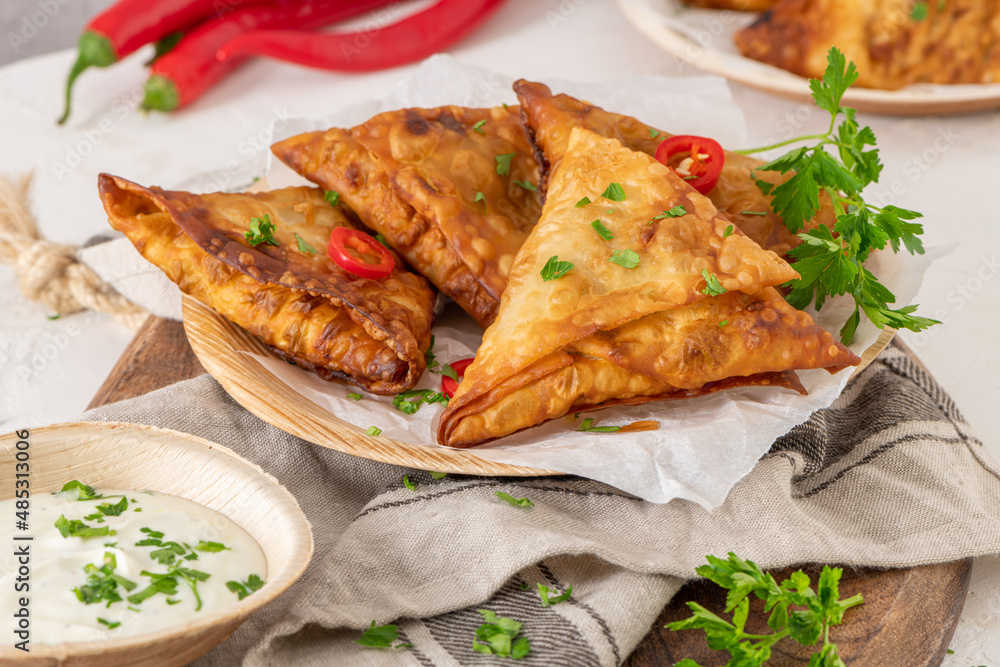 Indian samosas - fried or baked pastry with savoury filling, popular Indian snacks, served with yogurt sauce in areca leaf dishes with spices on kitchen countertop. Indian samosas - fried or baked pastry with savoury filling, popular Indian snacks, served with yogurt sauce in areca leaf dishes with spices on kitchen countertop.