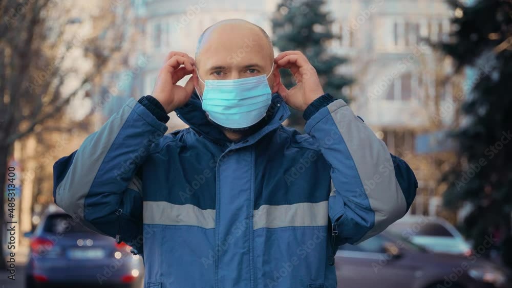 Man puts medical mask on his face to protecting himself from coronavirus pandemic and standing on street. Safe male practicing social distancing and COVID quarantine Man puts medical mask on his face to protecting himself from coronavirus pandemic and standing on street. Safe male practicing social distancing and COVID quarantine