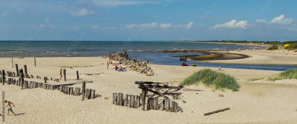 The mouth of the river Sventoji to the sea, the remains of an old bridge, sandy beach, people resting. Sea and blue sky.