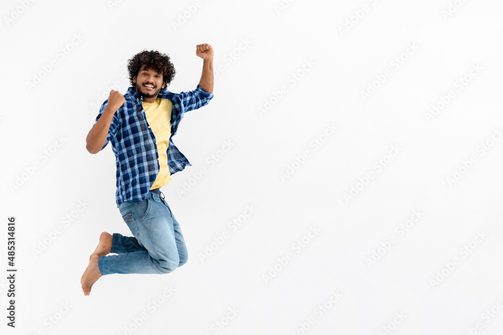 Cheerful Indian young man fun jumping on white background with copy space. Victory, celebrate triumph Cheerful Indian young man fun jumping on white background with copy space. Victory, celebrate triumph