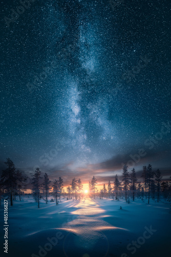 Beautiful sunrise over snowy forest with an epic milky way on the sky