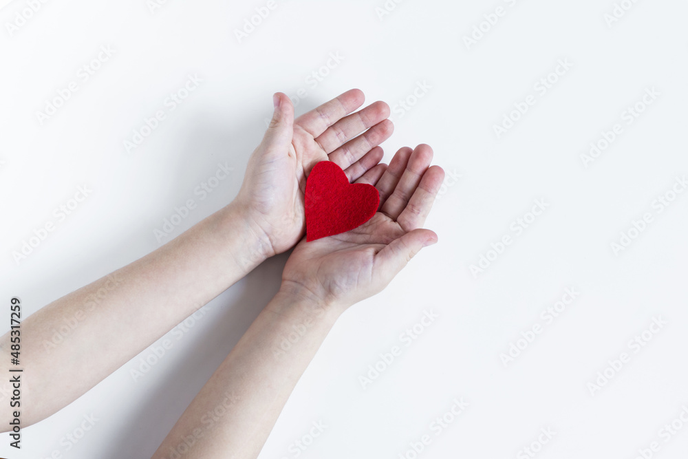 Children's open palms, holding a bright red heart on a light background. Children's open palms, holding a bright red heart on a light background.