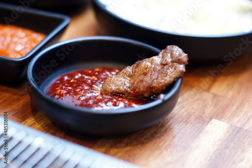 The grilled meat is dipped in red pepper paste sauce on a round plate.