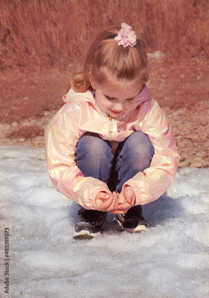 Child girl standing on melting snow with pieces of ice in springtime. investigate details of nature . outdoor kids activity and learning concept Child girl standing on melting snow with pieces of ice in springtime. investigate details of nature . outdoor kids activity and learning concept