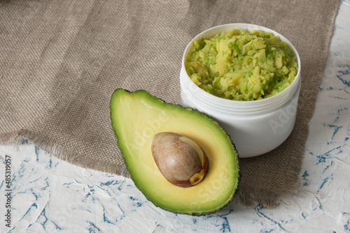 white mockup plastic jar with avocado puree, cut in half avocado and wooden comb photo