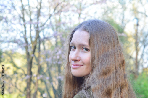 Beautiful young blonde woman with brown eyes and smile on her face in a blooming spring garden. Blurred background formed by blurred leaves, branches and flowers of cherry trees