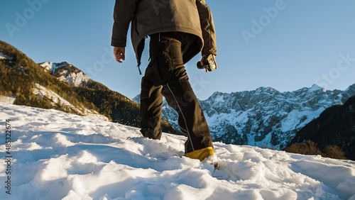 Young man reaching the mountain peak by hiking through the snow uphill.