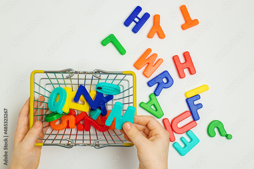 The child plays with colorful letters, collects letters in a metal basket. Education. English alphabet The child plays with colorful letters, collects letters in a metal basket. Education. English alphabet