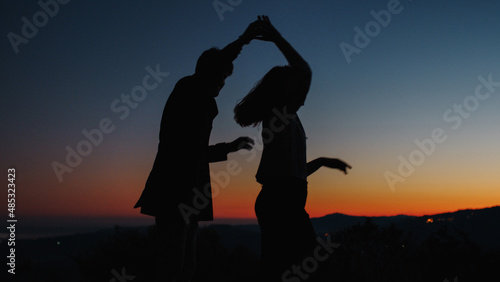 Silhouette of boy and girl cheerfully dance at sunset 