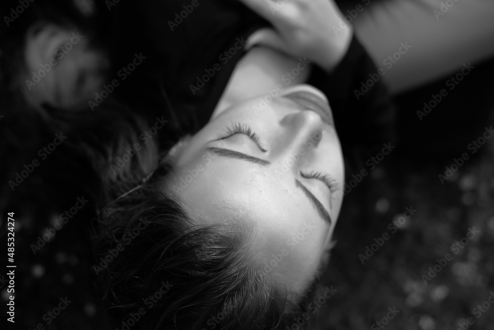 Black and white portrait of a young girl in the city park. Elegant and melancholy portrait, the girl is sitting on the grass. Beautiful woman in classic clothes