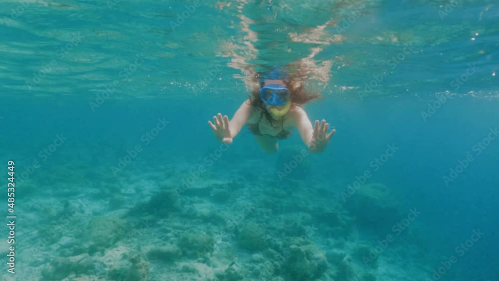 Woman in bikini shows peace sign swimming above coral reef Woman in bikini shows peace sign swimming above coral reef