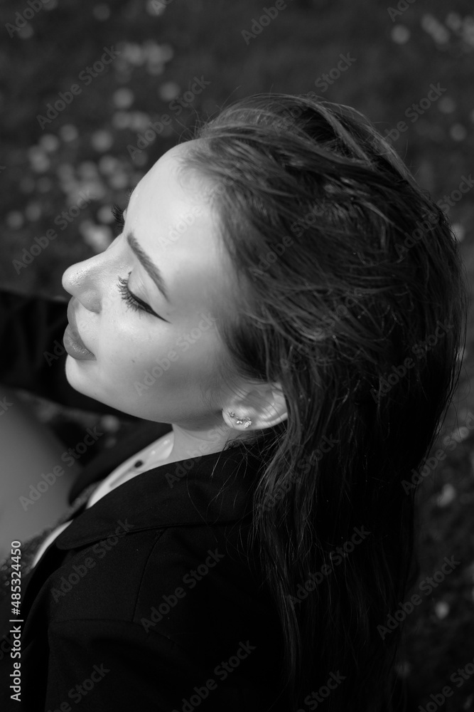 Black and white portrait of a young girl in the city park. Elegant and melancholy portrait, the girl is sitting on the grass. Beautiful woman in classic clothes Black and white portrait of a young girl in the city park. Elegant and melancholy portrait, the girl is sitting on the grass. Beautiful woman in classic clothes