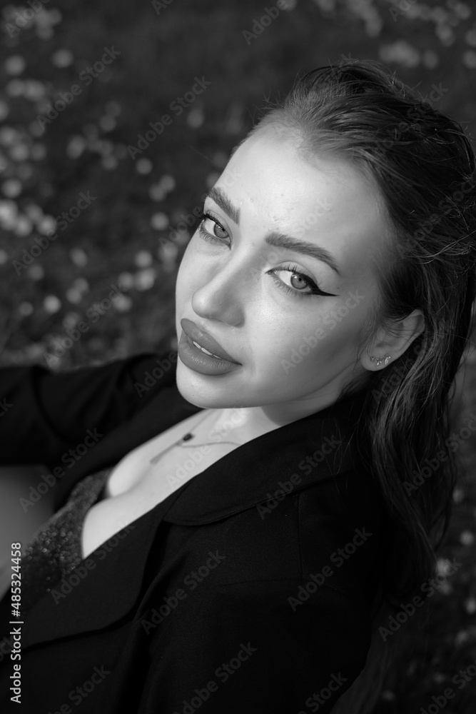 Black and white portrait of a young girl in the city park. Elegant and melancholy portrait, the girl is sitting on the grass. Beautiful woman in classic clothes Black and white portrait of a young girl in the city park. Elegant and melancholy portrait, the girl is sitting on the grass. Beautiful woman in classic clothes