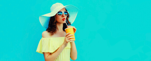 Portrait of beautiful young woman drinking a fresh juice wearing a summer hat on blue background