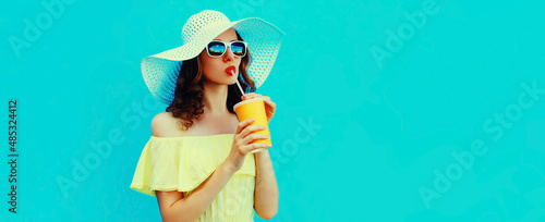 Portrait of beautiful young woman drinking a fresh juice wearing a summer hat on blue background