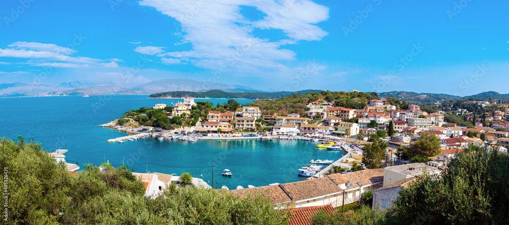 Panorama of Kassiopi town on Corfu island, Greece. Picturesque fishing village on rugged seashore with colorful houses, luxury villas and turquoise water. Popular tourist destination