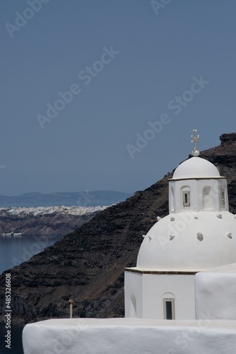 View of a beautiful whitewashed and traditional Orthodox Church, the volcanic landscape and the village of Oia in the background in Santorini Greece