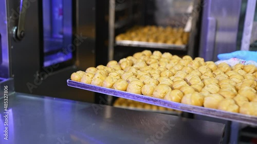 Freshly baked profitroles being taken off the oven. Factory worker pulls the baking sheet from oven and puts it on the table. Close up. photo