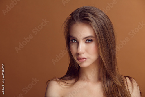 Seductive young woman with bare shoulders at brown wall