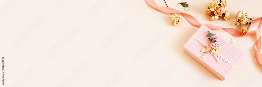 Beautiful pink gift box with dry roses flowers and ribbons on pastel background. Gift for holiday, birthday, Wedding, Mother's Day, Valentine's day, Women's Day. Copy space. Top view, flat lay. Banner Beautiful pink gift box with dry roses flowers and ribbons on pastel background. Gift for holiday, birthday, Wedding, Mother's Day, Valentine's day, Women's Day. Copy space. Top view, flat lay. Banner