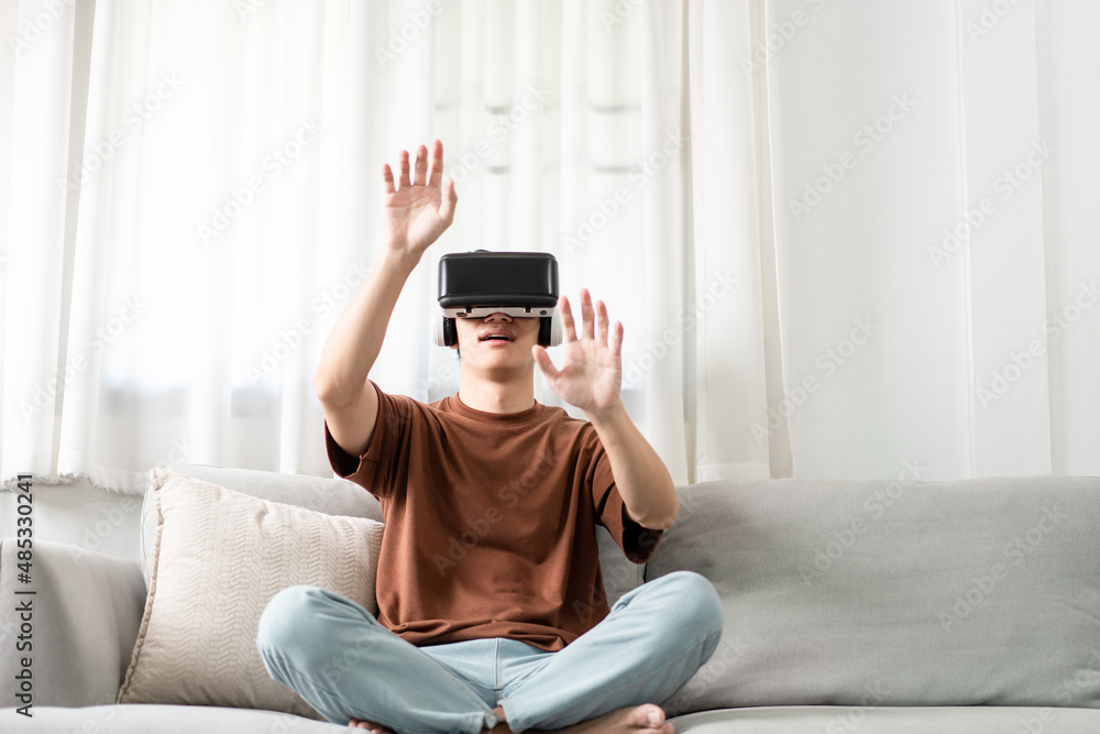 Technology Concept The man with his brown T-shirt and light blue jeans wearing a virtual reality headset while sitting on the sofa Technology Concept The man with his brown T-shirt and light blue jeans wearing a virtual reality headset while sitting on the sofa