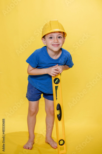 Little boy in yellow helmet builder with level tool