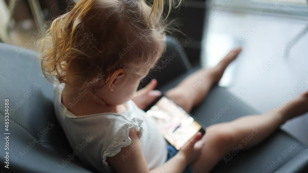Smiling little girl is sitting on armchair and using smart phone Smiling little girl is sitting on armchair and using smart phone