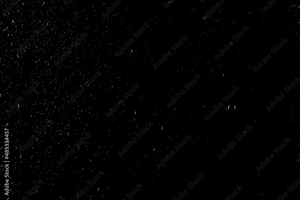 Drops of water flow down the surface of the clear glass on a black background. Texture for creativity.	