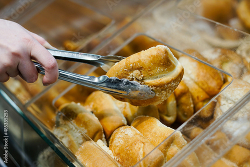 Photography Close up of woman takes fresh baked bun with tongs at a bakery store