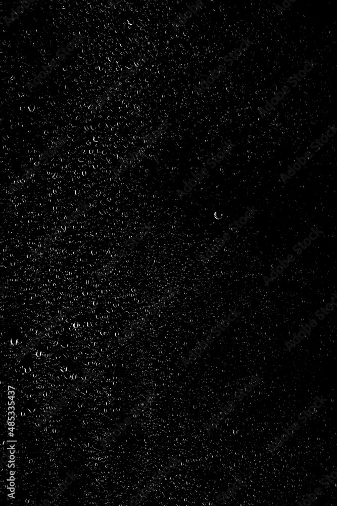 Drops of water flow down the surface of the clear glass on a black background. Vertical orientation. Texture for creativity.