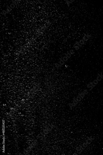 Drops of water flow down the surface of the clear glass on a black background. Vertical orientation. Texture for creativity.