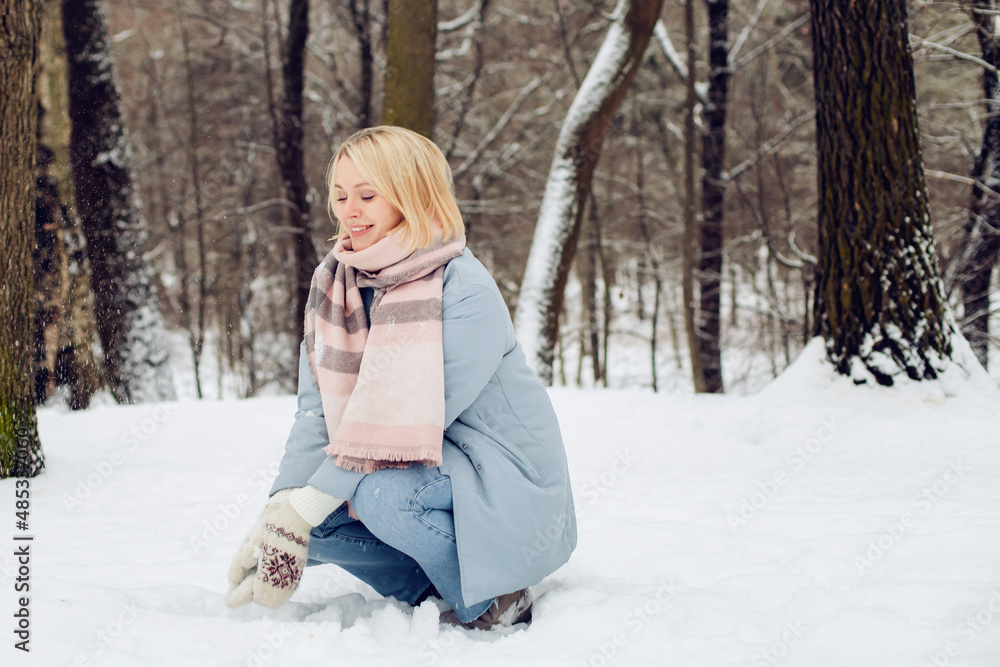 Fototapeta premium Outdoors portrait of young beautiful woman girl with blond hair and blue warmcoat having fun and smile in winter park