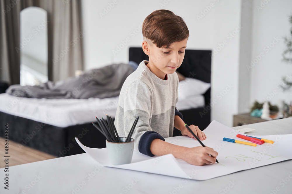 Concentrated child boy sitting at the table and drawing surprise for his lovely father Concentrated child boy sitting at the table and drawing surprise for his lovely father