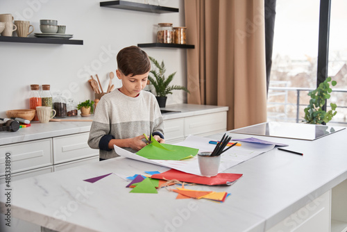 Boy cutting carton by scissors and smiling while preparing present for his father