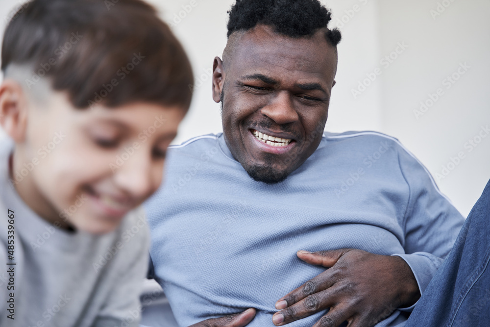 Multiracial man smiling toothy while looking how his son drawing at home during the weekend Multiracial man smiling toothy while looking how his son drawing at home during the weekend